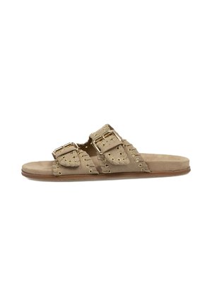Sandalias deslizantes de ante beige con dos correas de hebilla doradas, que presentan un diseño recortado y con tachuelas a lo largo de los bordes y una suela plana.