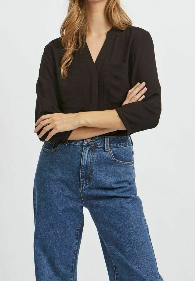 Blusa nera a maniche lunghe con scollatura a V e tasca frontale, abbinata a jeans in denim a lavaggio medio e fit morbido.