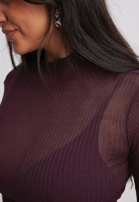 Burgundia soonik kõrge kaelusega; omab läbipaistvaid paneele õlgadel ja tekstureeritud pinda. Täiendatud kõrvarõngastega.