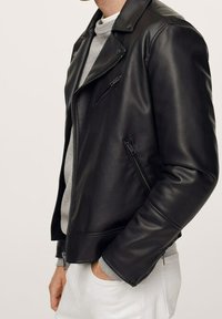 Giacca da motociclista in pelle nera con design aderente, cerniera frontale asimmetrica e tasche con zip. Caratterizzata da una texture liscia e colletto con intagli.