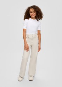 Weißes Kurzarmhemd mit Ausschnittdetails, kombiniert mit cremefarbenen Weitbeinen und weißen Sneakers. Glatter Stoff, lässige Passform und neutrale Farben.