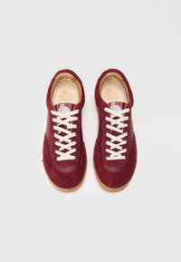 Burgunderfargede sneakers med teksturert stoffoverdel og glatte skinnaksenter. Har hvite lisser og en gummisåle. Perforerte detaljer er til stede.