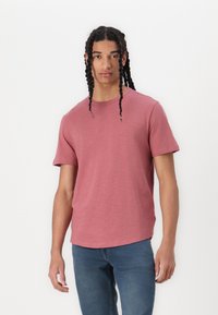 Korte mouwen, ronde hals T-shirt in een verouderde rozenkleur, gemaakt van zacht materiaal met een lichte textuur. Gepaard met blauwe spijkerbroek.