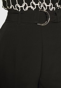 Czarne, wysokiej talii spodnie z szerokim paskiem z okrągłą srebrną klamrą, gładką teksturą i czystymi liniami bez widocznych kieszeni.