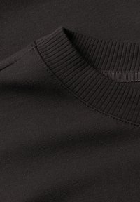 Gros plan d'un pull noir encolure ronde montrant le col côtelé et la texture fine du tissu en maille.
