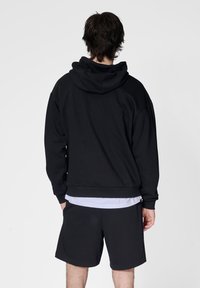Zwarte hoodie met geribde manchetten en zoom, met een comfortabele pasvorm. Gecombineerd met zwarte shorts, gezien van achteren tegen een effen achtergrond.