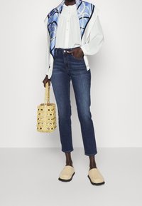 Bílá blůzka s knoflíkovou légou, modrý vzorovaný šátek, tmavé džíny, béžové espadrilky a žlutá tkaná kabelka s řetízkovým uchem.