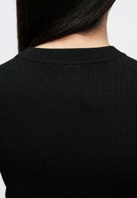 Top negru cu dungi, cu decolteu rotund și țesătură texturată, cu cusături vizibile de-a lungul decolteului pentru detalii suplimentare.