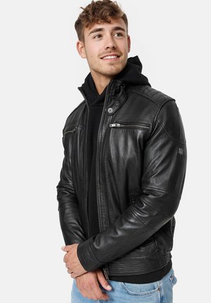 Giacca in pelle nera con zip frontale, due tasche sul petto, polsini e spalle a coste. Indossata sopra un hoodie nero, con una trama liscia.