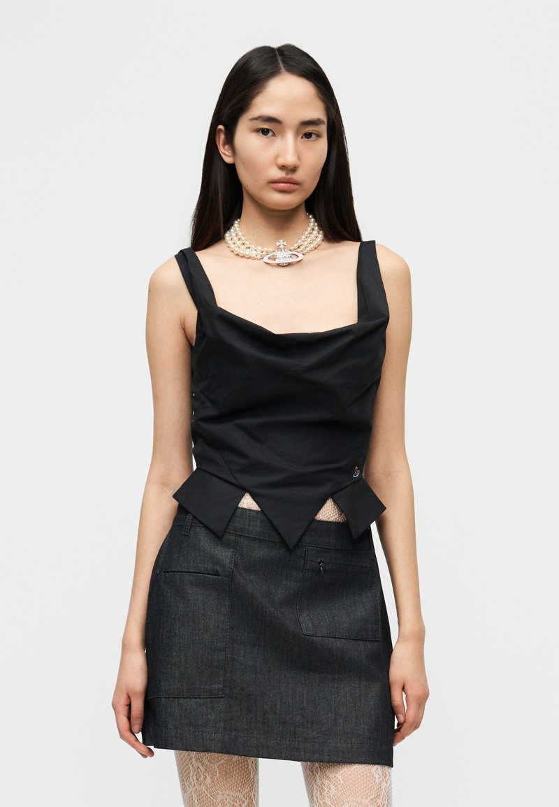 Μαύρο αμάνικο τοπ με δομητή υφή, φα ρδύ ντεκολτέ και αιχμηρό τελείωμα, συνδυασμένο με σκούρα μίνι φούστα από τζιν. Κολιέ από πέρλες με καρφίτσα.