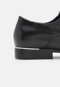 Chaussure en cuir noir avec un bout arrondi et un talon carré bas. Présente un accent métallique argenté sur le talon et une texture lisse.