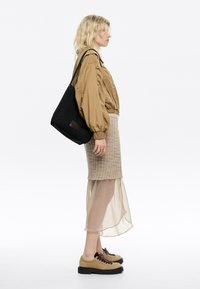 Bežinė bomber tipo striukė, megzta bežinė sijonas su permatomu sluoksniu, juoda hobo tipo rankinė ir bežinės spalvos batai su tamsiomis raišteliais ir storomis padais.