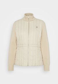 Jasno beżowa kurtka zapinana na zamek, łącząca pikowany nylonowy przód z dzianinowymi rękawami, z wysokim kołnierzem i naszywką z logo.
