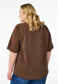 Haut marron à manches courtes avec une coupe décontractée, un tissu texturé et un ourlet arrondi, associé à un jean en denim bleu.