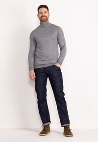 Grauer Rollkragenpullover, eng anliegend, mit langen Ärmeln; kombiniert mit dunklen Jeans im geraden Schnitt, mit hochgerollten Säumen, getragen mit braunen Wildlederstiefeln.