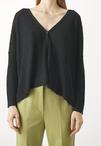 Svart ribbade stickade cardigan med djup V-ringning, framknappar och en lös siluett, tillsammans med ljusgröna högmidjade byxor.