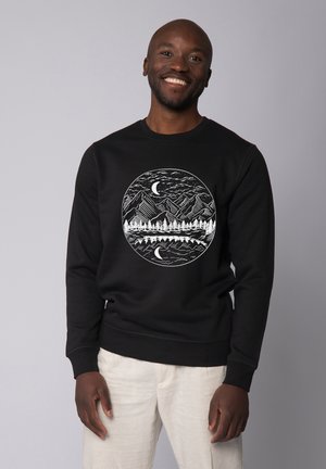Pull noir avec un motif circulaire blanc représentant des montagnes, des arbres et des lunes. Fabriqué en coton avec une texture lisse et des poignets côtelés.