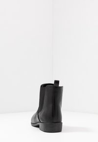 Stivaletto alla caviglia in pelle nera con pannelli laterali elastici, punta arrotondata, tacco basso a blocco e linguetta posteriore. Texture liscia con dettagli di cucitura.
