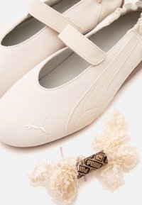 Chaussures style Mary Jane crème Puma avec une bride et un accessoire décoratif pour cheveux en dentelle assorti avec le logo Puma.