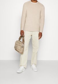 Beige ribbad tröja, krämfärgade byxor och vita sneakers. Håller en liten beige tygväska med rem och silverfärgade detaljer.