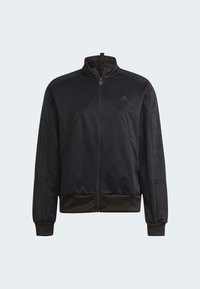 Chaqueta negra con cremallera, hecha de un tejido suave, con cuello alto, corte atlético, paneles laterales texturizados y tres franjas en las mangas.