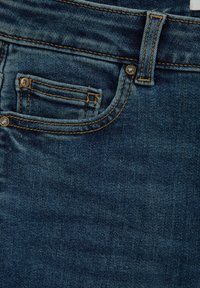 Modré džíny z denimu mají malou přední kapsu, viditelné švy v kontrastní žluté barvě a kovové zapínání na knoflík. Povrch je hladký.