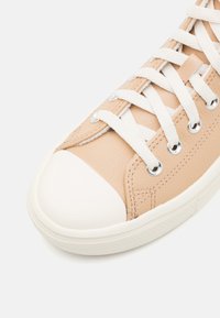 Baskets en cuir tan avec un capuchon en caoutchouc blanc sur le bout et une semelle blanche. Dotées de lacets blancs et d'œillets en métal avec des détails de couture visibles.