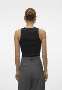 Top negro sin mangas con un diseño ajustado, combinado con pantalones grises de tiro alto que tienen dobles bolsillos traseros y lazos laterales para cinturón.