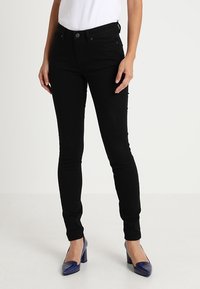 Jeans negros ajustados de mezclilla elástica, con un ajuste clásico, cinco bolsillos y una textura sutil, combinados con tacones azules de charol.