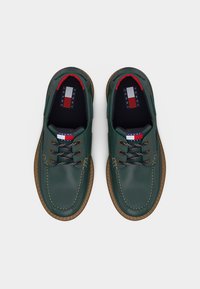 Ζευγάρι πράσινα δερμάτινα casual παπούτσια με κορδόνια, καφέ σόλες και λογότυπο Tommy Jeans στη γλώσσα και την εσωτερική σόλα, σε θέα από πάνω.