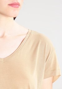 T-shirt in cotone beige con scollo a V e maniche corte. Il tessuto appare morbido con una superficie liscia e leggera elasticità, caratterizzato da un colletto pulito.