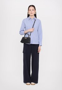 Chemise rayée bleue à boutons, associée à un pantalon navy ample avec poches latérales, et un petit sac à main noir.