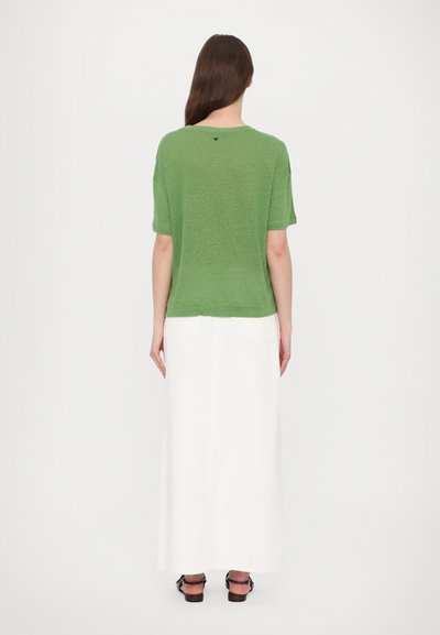 Top verde a maniche corte realizzato in materiale leggero, abbinato a una lunga gonna bianca. Il top presenta un colletto arrotondato e una vestibilità ampia.