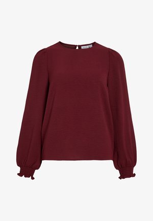 Top color bordeaux con maniche lunghe a palloncino, scollatura rotonda e chiusura a occhio di bue sul retro. Tessuto testurizzato con polsini arricciati e elasticizzati.