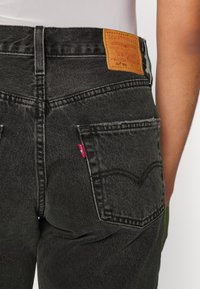 Schwarze Denim-Jeans mit einem markierten Lederpatch nahe dem Bund, ausgestattet mit Gesäßtaschen, die kontrastierende Nähte und ein rotes Etikett aufweisen.