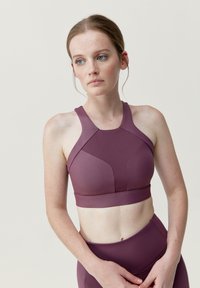 Bordeauxfärgad sportbh med hög halsringning och racerback-design, utrustad med vadderade kupor och ett mjukt, stretchigt tyg. Sömlösa detaljer förbättrar passformen.