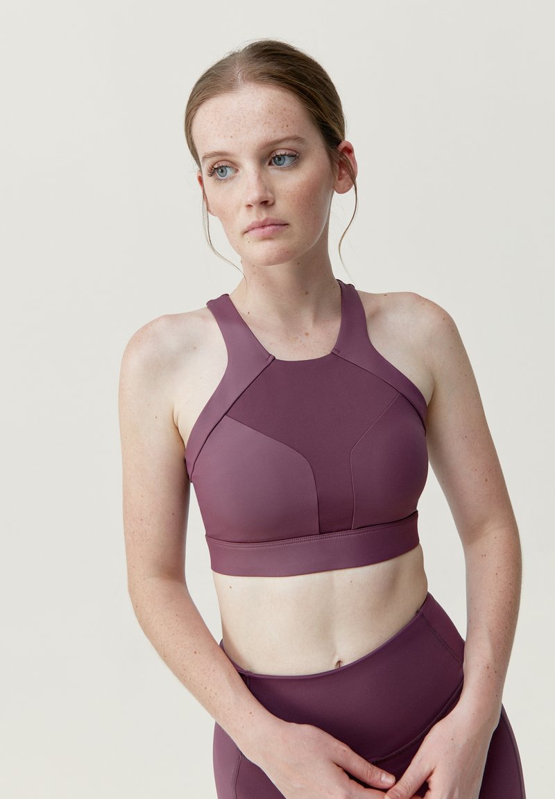 Bordeauxfärgad sportbh med hög halsringning och racerback-design, utrustad med vadderade kupor och ett mjukt, stretchigt tyg. Sömlösa detaljer förbättrar passformen.