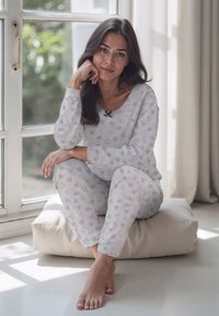 Harmaa pyjama-setti, jossa on sydänkuvioita, sisältää väljän paidan ja yhteensopivat housut, joissa on elastiset hihnat. Pehmeä kangas ja rento malli.