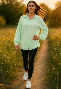 Camicia verde chiaro con maniche lunghe, leggings neri e sneakers bianche; camminando su un sentiero circondato da fiori gialli.