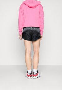 Bermudas de satén negras con un corte suelto, que cuentan con una cintura elástica, combinadas con una sudadera corta de color rosa brillante y zapatillas deportivas multicolores.