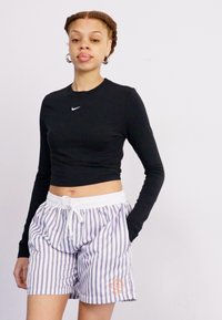 Svart langermet crop topp med Nike-logo, kombinert med stripete shorts med elastisk liv og oransje grafisk detalj.
