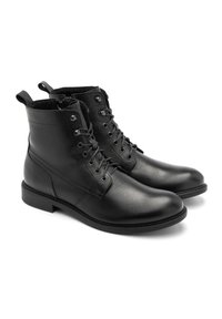 Botas negras de cuero con cordones, con un acabado texturizado, punteras redondas y ojales de metal. Altura de tobillo con tiradores para facilitar el calzado.