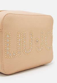 Borsa in pelle color pesca con decorazioni in oro e strass che formano il nome del marchio. Texture liscia con forma rettangolare.