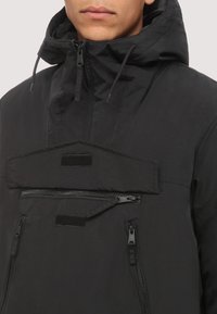 Chaqueta negra ligera con capucha, un bolsillo horizontal con cremallera y dos cremalleras laterales. Textura suave con detalles de diseño minimalistas.