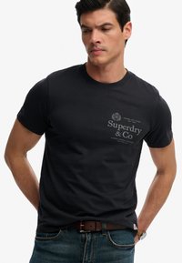 Czarny bawełniany t-shirt z okrągłym dekoltem, krótkimi rękawami i nadrukowanym szarym logo "Superdry & Co" w kontrastowym kolorze.