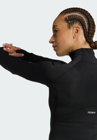 Crna dugorukava atletska majica od rastezljivog materijala, s visokim ovratnikom, bešavnim ramenima i malim "TECHFIT" logotipom sa strane.