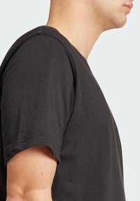 Černé bavlněné tričko s krátkými rukávy, kulatým výstřihem a volným střihem. Má hladkou texturu a jednoduchý design.