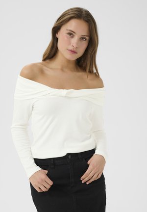 Weißes, geripptes Langarmoberteil mit schulterfreiem Design und Frontknoten, kombiniert mit einem schwarzen Rock, der eine körpernahe Passform und eine weiche Textur aufweist.