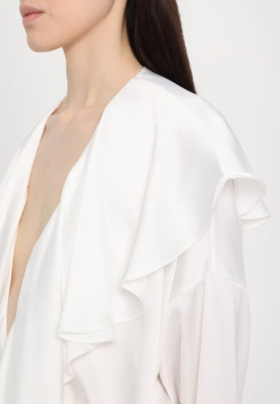 Witte zijden blouse met een diepe V-hals en gelaagd gerimpeld kant langs de schouders. Een gladde textuur met een zachte glans.