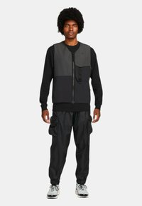 Svart och grå zip-front jacka med en stor ficka och dragsko byxor. Båda har en mjuk textur och en avslappnad passform.